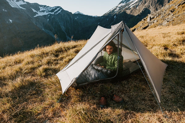 Gossamer Gear The One V2 – hiker sitting inside on a grassy hillside with mountains behind, boots outside