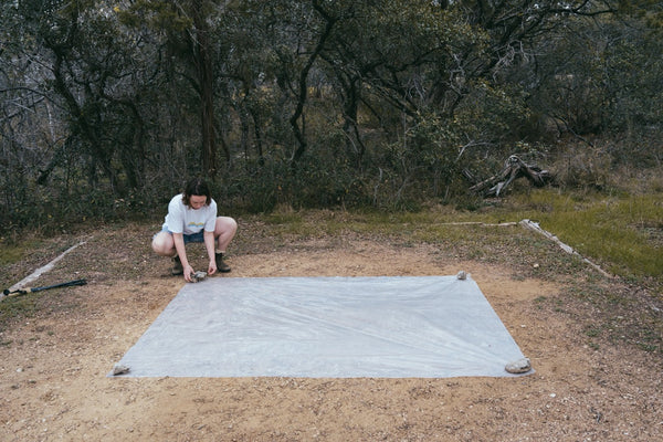 Gossamer Gear Polycro Ground Cloth laid flat on dirt, hiker staking a corner