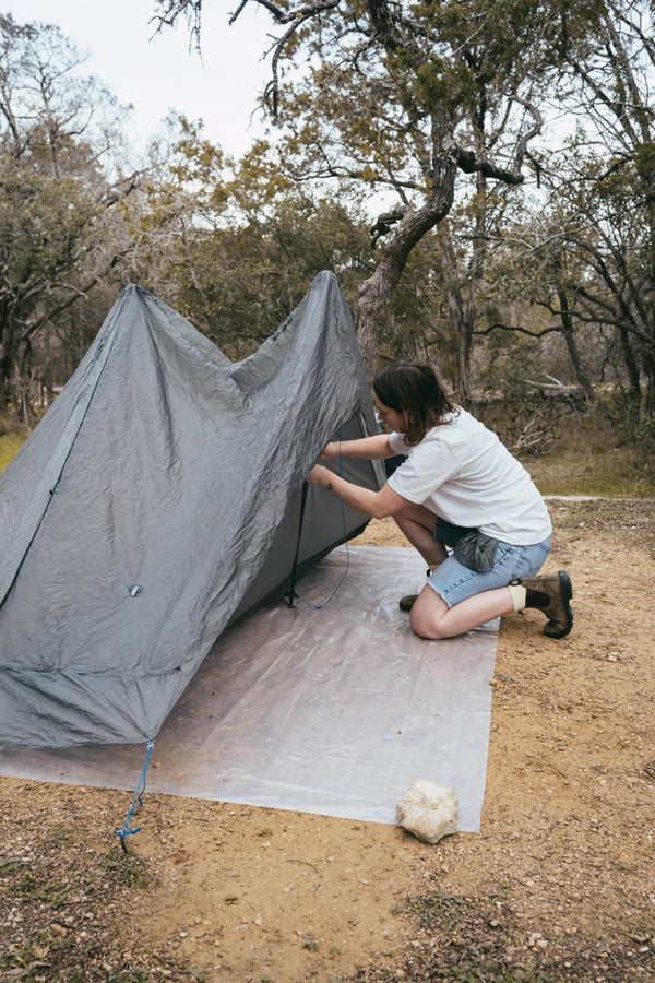 Gossamer Gear Polycro Ground Cloth under a pitched tent, hiker adjusting the corner stake